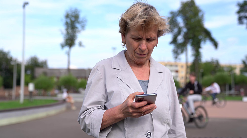 An-older-focused-woman-writes-a-message-on-her-brand-new-smartphone-walking-on-the-street.---v---ss-feat