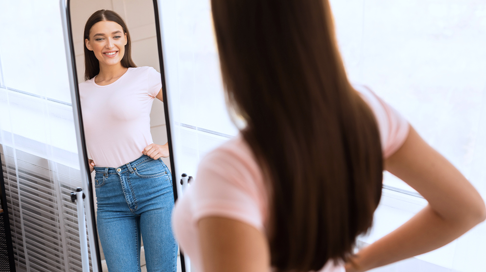 PH-Cheerful Fit Woman Looking At Reflection In Mirror Standing Indoor-ssWhat Is Brown Fat _ How It Improves Metabolism-Feature