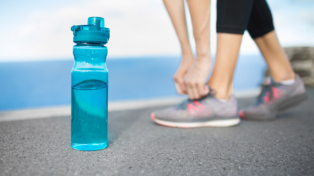 Active-female-runner-tying-shoe-next-to-bottle-of-water-How-Does-Dehydration-Affect-the-Physical-and-Cognitive-Performance-of-Athletes