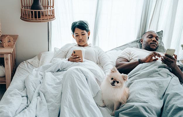 multiracial-couple-surfing-mobile-phones-lying-in-bed-with-dog-after-awakening-What-Can-Affect-Your-Biological-Age-Test-Result